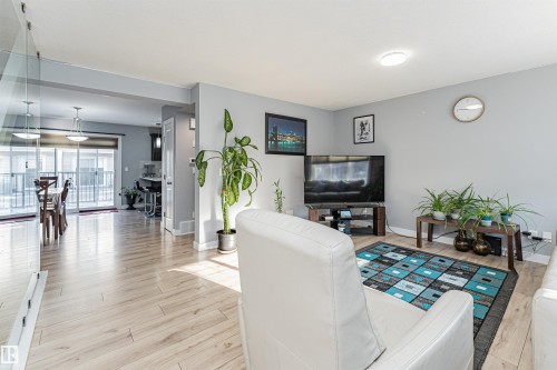 Open concept living area featuring light wood-finish flooring, recessed lighting, and a glass partition - 35 675 Albany Way, Edmonton, AB 