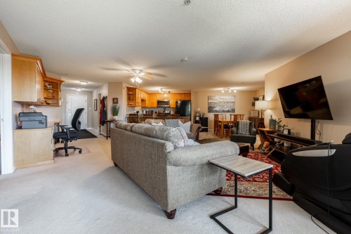 Open-concept living area featuring light-toned carpeting, a built-in office area with wood cabinetry, and a kitchen with wood-finish cabinetry - 330 1520 Hammond Gate Gate, Edmonton, AB 