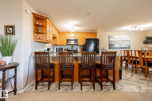 Open-concept kitchen featuring light wood cabinetry, a granite-finish countertop, and stainless steel appliances - 330 1520 Hammond Gate Gate, Edmonton, AB 