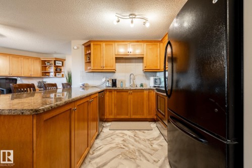 Kitchen featuring wood cabinetry, light-toned countertops, a black refrigerator, and patterned floor tile - 330 1520 Hammond Gate Gate, Edmonton, AB 