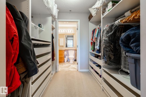 Walk-through closet featuring built-in shelving, hanging rods, and integrated drawers, leading to a bathroom with a wood-finish vanity and tiled flooring - 330 1520 Hammond Gate Gate, Edmonton, AB 