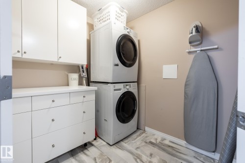 Dedicated laundry area featuring stacked appliances, extensive white cabinetry, a built-in countertop, wall-mounted ironing board storage, and wood-finish flooring - 330 1520 Hammond Gate Gate, Edmonton, AB 