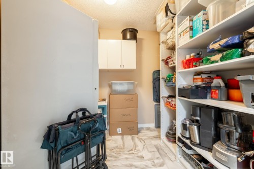 Walk-in pantry featuring extensive built-in shelving, white cabinetry, a flush-mount ceiling light, and light-toned tile flooring - 330 1520 Hammond Gate Gate, Edmonton, AB 