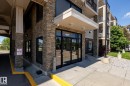Building entrance featuring stacked stone facade, large glass double doors, covered drop-off area, and concrete pathways - 330 1520 Hammond Gate Gate, Edmonton, AB 