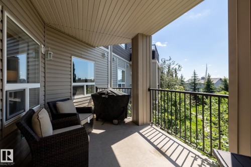 Covered concrete patio featuring dark metal railings and a verdant treeline backdrop - 330 1520 Hammond Gate Gate, Edmonton, AB 