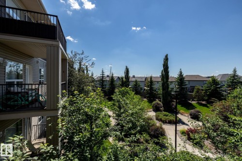 Private balcony with black railing overlooking a landscaped parkway featuring mature trees, paved pathways, and green spaces - 330 1520 Hammond Gate Gate, Edmonton, AB 