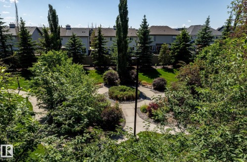 Landscaped communal green space featuring a winding paved pathway, mature trees, manicured lawns, and built-in benches - 330 1520 Hammond Gate Gate, Edmonton, AB 