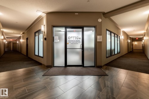 Commercial space entry featuring frosted glass doors, large window panels, wood-finish tile flooring, recessed ceiling lighting, and wall-mounted sconces - 330 1520 Hammond Gate Gate, Edmonton, AB 