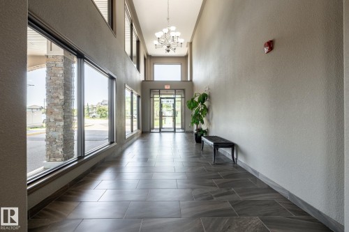 Spacious entryway featuring large format tile flooring, expansive windows, a multi-tiered chandelier, and a stone-clad column - 330 1520 Hammond Gate Gate, Edmonton, AB 