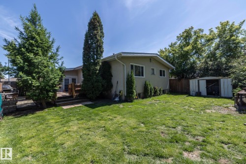 Expansive green lawn with mature evergreen trees and a raised wooden deck - 3608 44 Street, Leduc, AB 