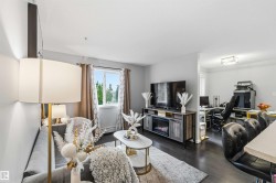 Living space with dark wood-finish flooring, a contemporary electric fireplace media console, and a large window providing ample natural light - 