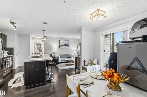 Open-concept living area featuring wood-finish flooring, a kitchen island with seating, stainless steel appliances, a sliding glass door, and recessed lighting - 244 1196 Hyndman Road, Edmonton, AB 