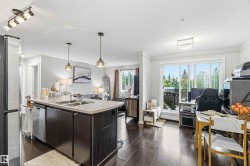Open-concept living area featuring a kitchen island with integrated sink, dark wood-finish flooring, recessed lighting, and large sliding glass doors leading to an exterior balcony - 