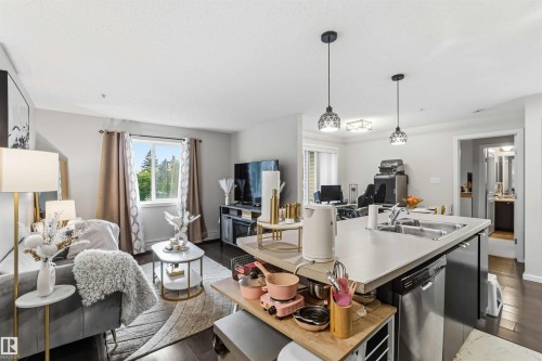 Open-concept living space featuring wood-finish flooring, a kitchen island with integrated sink, and stainless steel dishwasher - 244 1196 Hyndman Road, Edmonton, AB 