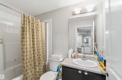 Bathroom featuring a white bathtub with subway tile surround, dark wood-finish vanity with a light countertop, integrated sink, and an overhead two-bulb light fixture - 