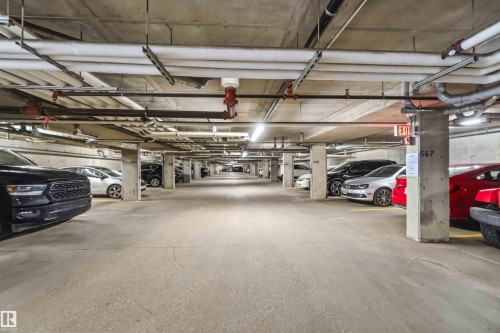 Underground parking garage featuring concrete pillars and ceiling, overhead exposed utility lines, and fluorescent lighting - 244 1196 Hyndman Road, Edmonton, AB 