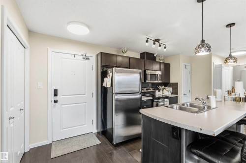Kitchen featuring dark wood-finish cabinetry, stainless steel appliances, and a light-colored countertop with an integrated double sink - 244 1196 Hyndman Road, Edmonton, AB 