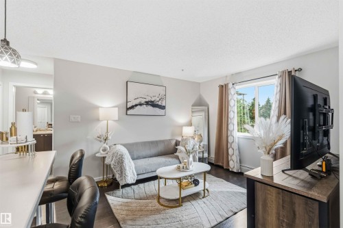 Open concept living area featuring dark wood-finish flooring, a large window, and light gray wall paint - 244 1196 Hyndman Road, Edmonton, AB 