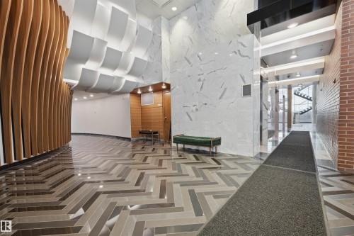 Lobby featuring a herringbone pattern floor, curved wood-panel wall, recessed lighting, and a white marble-look accent wall - 802 9720 106 Street, Edmonton, AB 