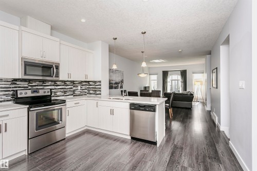 Modern kitchen featuring white cabinetry, stainless steel appliances, a mosaic tile backsplash, and light-toned countertops - #55 723 172 St Sw, Edmonton, AB - Indoor Photo Showing Kitchen With Upgraded Kitchen