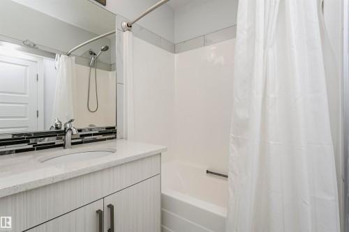 Bathroom featuring a white bathtub with a shower combination, a chrome shower head with handheld sprayer, a vanity with a white countertop and integrated sink, a mosaic tile backsplash, and a large mirror - #55 723 172 St Sw, Edmonton, AB - Indoor Photo Showing Bathroom