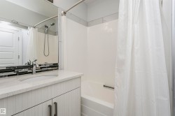 Bathroom featuring a white bathtub with a shower combination, a chrome shower head with handheld sprayer, a vanity with a white countertop and integrated sink, a mosaic tile backsplash, and a large mirror - 
