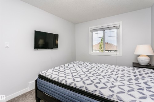 Carpeted room featuring light gray walls, a window with white trim, and a wall-mounted television - #55 723 172 St Sw, Edmonton, AB - Indoor Photo Showing Bedroom