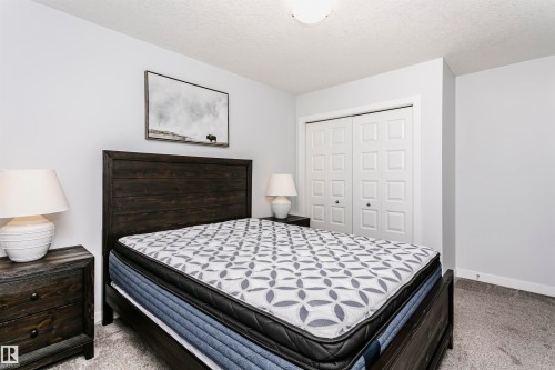 Room featuring light gray wall paint, textured ceiling, light gray carpet flooring, and white bi-fold closet doors - #55 723 172 St Sw, Edmonton, AB - Indoor Photo Showing Bedroom