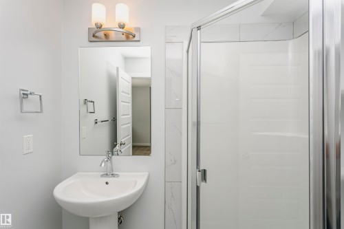 Modern bathroom featuring a pedestal sink, chrome faucet, and a rectangular mirror - #55 723 172 St Sw, Edmonton, AB - Indoor Photo Showing Bathroom