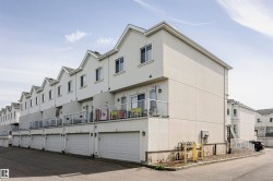Modern townhome exterior featuring an attached garage, private balcony with glass railing, stucco facade, and pitched rooflines - 