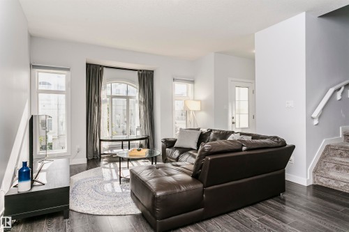 Living area featuring dark wood-finish flooring, light gray wall paint, and a carpeted staircase with white railings - #55 723 172 St Sw, Edmonton, AB - Indoor Photo Showing Living Room