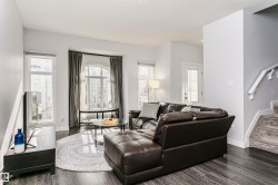 Living area featuring dark wood-finish flooring, light gray wall paint, and a carpeted staircase with white railings - 