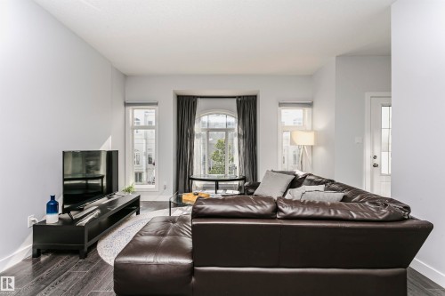 Living area featuring wood-finish flooring, light grey walls, and a prominent bay window with an arched transom - #55 723 172 St Sw, Edmonton, AB - Indoor Photo Showing Living Room