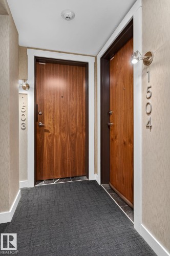 Hallway featuring two wood-finish entry doors with dark frames, white trim, and polished chrome hardware - 1504 9720 106 Street, Edmonton, AB 