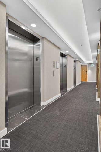 Hallway featuring multiple stainless steel elevators, inset ceiling lighting, textured wall coverings, and patterned carpeting - 1504 9720 106 Street, Edmonton, AB 