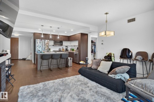 Open-concept living space featuring wood-finish flooring, a contemporary kitchen, stainless steel appliances, a kitchen island with seating, and recessed lighting - 1504 9720 106 Street, Edmonton, AB 
