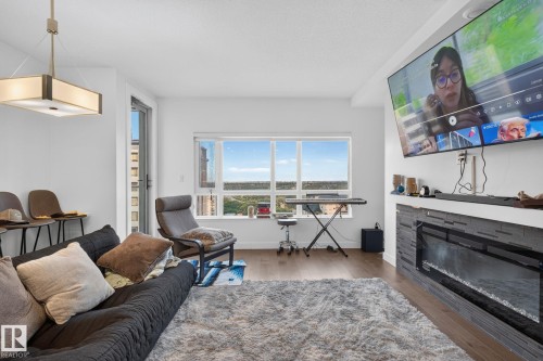 Open-concept living space featuring wood-finish flooring, a contemporary linear fireplace with a textured stone surround, and an expansive window - 1504 9720 106 Street, Edmonton, AB 