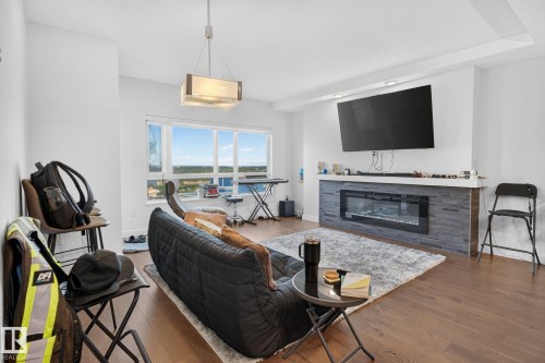 Living area featuring expansive windows, wood-finish flooring, and a contemporary fireplace with a stone-tile surround - 1504 9720 106 Street, Edmonton, AB 