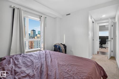 White walls and carpeted flooring define this room, featuring a large window with a cityscape background - 1504 9720 106 Street, Edmonton, AB 