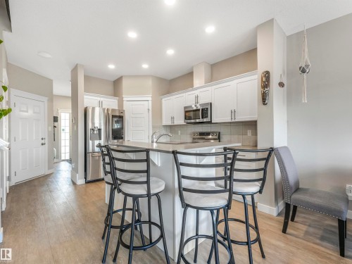 Modern kitchen featuring white cabinetry, stainless steel appliances, a center island with bar seating, recessed lighting, and wood-finish flooring - 17171 38 Street, Edmonton, AB 