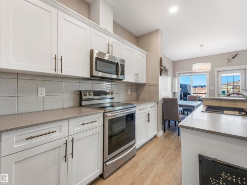 Modern kitchen featuring white shaker cabinetry, stainless steel appliances, light gray countertops, and a patterned tile backsplash - 17171 38 Street, Edmonton, AB 