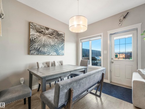 Bright dining area featuring wood-finish flooring, a contemporary drum pendant light fixture, and a white paneled door with grid-patterned glass - 17171 38 Street, Edmonton, AB 
