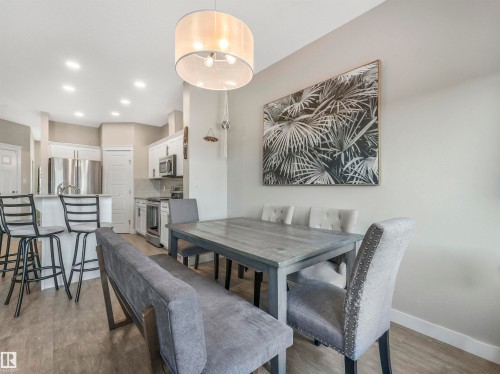 Open concept living area featuring wood-finish flooring, recessed lighting, a kitchen with white cabinetry, stainless steel appliances, and a breakfast bar - 17171 38 Street, Edmonton, AB 
