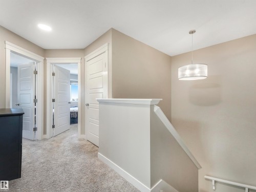 Upper-level hallway featuring plush gray carpeting, contemporary five-panel interior doors, and a decorative drum pendant light fixture - 17171 38 Street, Edmonton, AB 