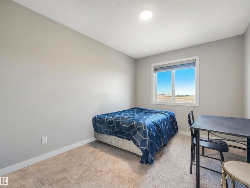 Carpeted bedroom featuring a large window, neutral wall paint, and white baseboards - 17171 38 Street, Edmonton, AB 