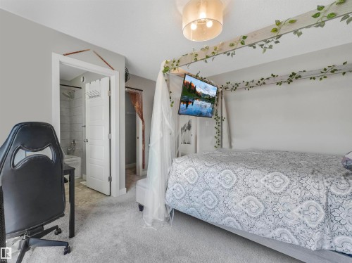 Carpeted bedroom with a built-in wall-mounted television, an open doorway revealing a tiled shower, and a secondary open doorway - 17171 38 Street, Edmonton, AB 