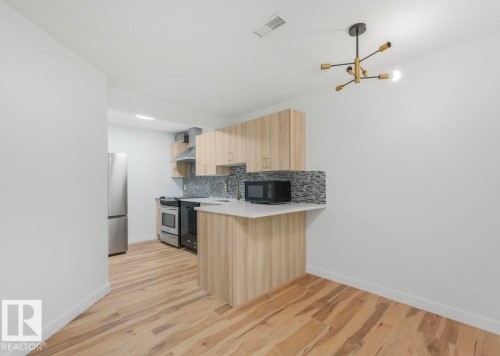 Modern kitchen featuring light wood-finish cabinetry, stainless steel appliances, a mosaic tile backsplash, and light-toned countertops - 17171 38 Street, Edmonton, AB 