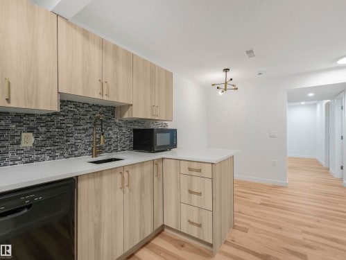 Kitchenette featuring light wood-finish cabinetry, a mosaic tile backsplash, white countertops, a black dishwasher, and a gold-finish faucet - 17171 38 Street, Edmonton, AB 