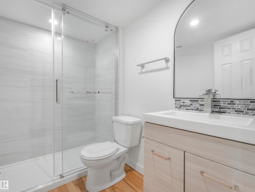 Bathroom featuring a glass-enclosed shower with white tiled walls, a light wood-finish vanity with a white countertop sink, and a mosaic tile backsplash - 17171 38 Street, Edmonton, AB 