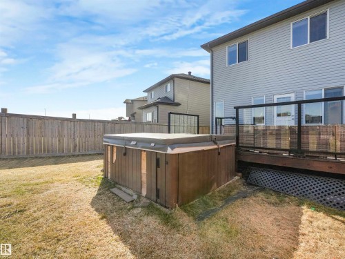 Private backyard featuring a wood-finish hot tub, wood privacy fence, and a raised wood deck with glass panel railing - 17171 38 Street, Edmonton, AB 